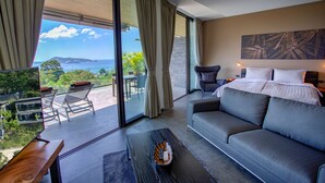 A modern hotel room with a large bed, a sofa, a dining table, and a view of the ocean. - Ocean Rock Kalim (Patong)