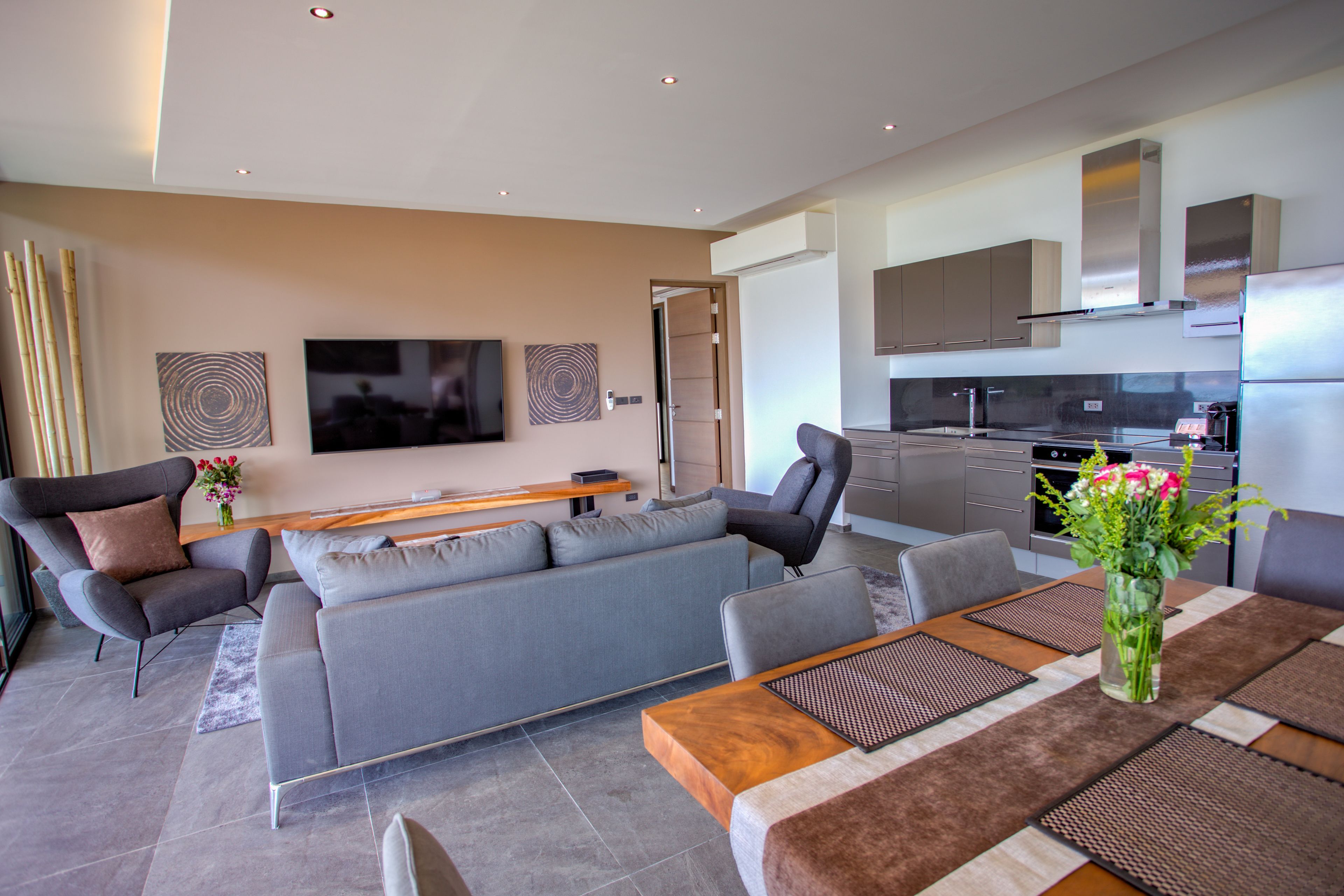 A modern living room with a grey sofa, a wooden coffee table, and a TV mounted on the wall.