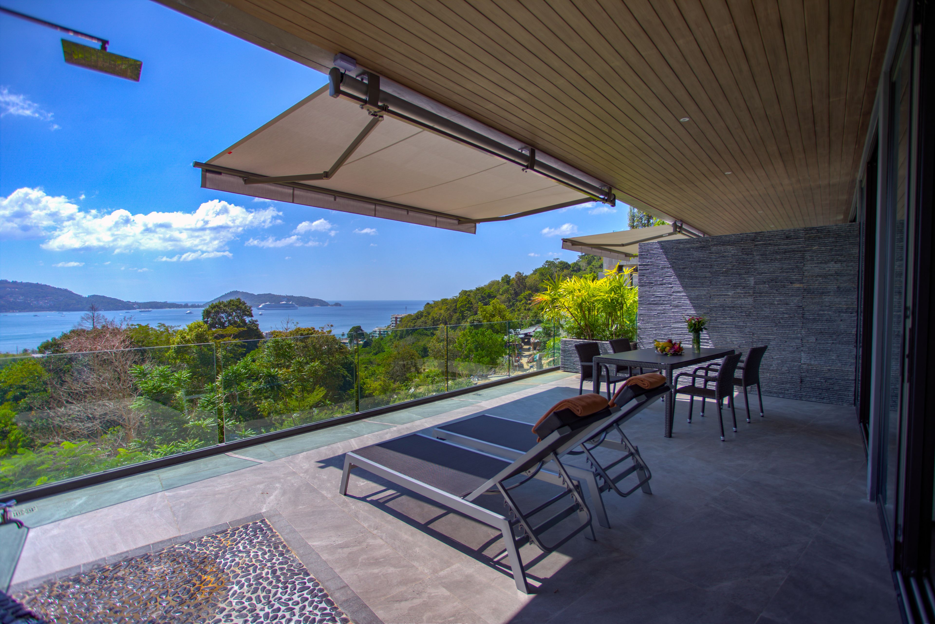 A balcony with a view of the sea, a table with chairs, and a lounge chair.
