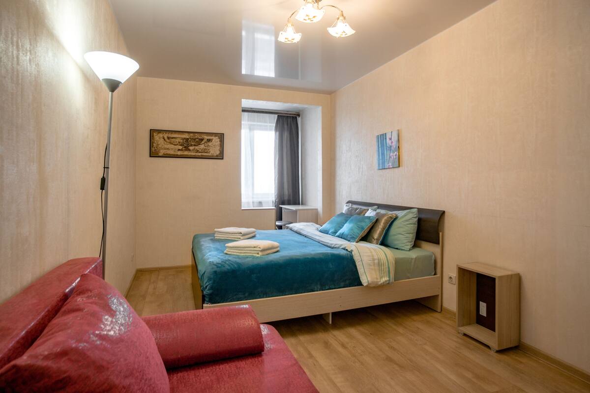 A bedroom with a bed, a bedside table, a lamp, a window, and a painting on the wall.