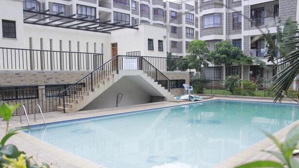 A swimming pool with a staircase leading to a balcony, surrounded by a multi-story building with balconies and a garden area. - Apple Residdence (Syokimau)