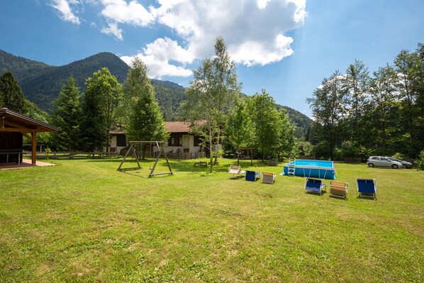 A grassy outdoor area with a swing set, a pool, and a covered seating area. - Apartment surrounded by greenery in Val Concei (Ledro)
