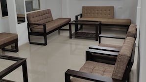 Een moderne woonkamer met een bank, fauteuils en salontafels. Er is een plafondventilator en een wandplank.
