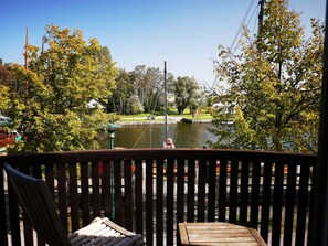 Una terraza con vistas a un lago, rodeada de árboles y un muelle con barcos.