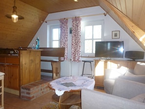 Une pièce mansardée chaleureuse avec un plafond en bois, une télévision, une table à manger avec des chaises et un canapé.