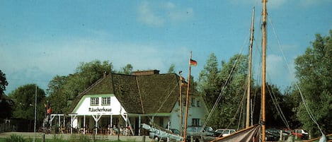 A traditional building with a sign 'Raucherhaus' by a calm water body with a sailboat docked.