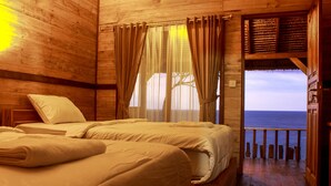 Camera da letto in una baita di legno con due letti, un balcone con ringhiera e vista sull'oceano.