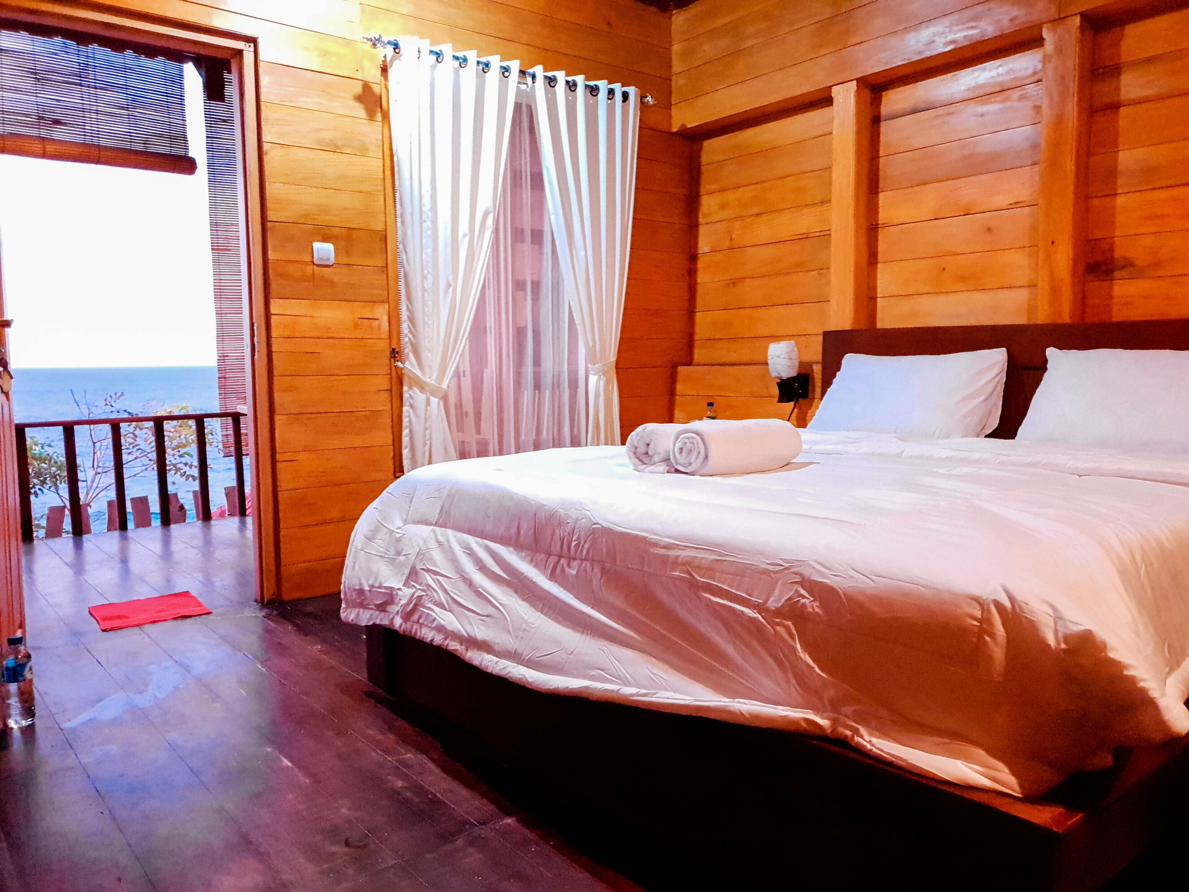 Habitación de una cabaña de madera con una cama, un tapete rojo, una botella y vista al océano.