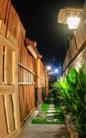 Un estrecho sendero bordeado por edificios de madera con techo de paja, que conduce a una zona bien iluminada.