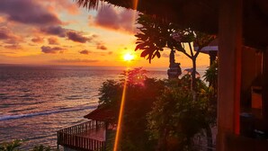 Tramonto sull'oceano con una terrazza in legno e vegetazione tropicale.