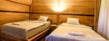 Dos camas individuales con cabeceros de madera y ropa de cama blanca en una habitación tipo cabaña con paredes de madera y una mesita de noche entre ellas.