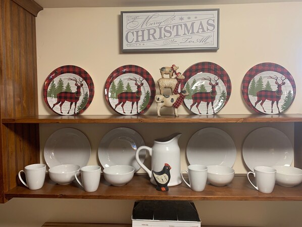 A kitchen shelf with decorative plates and a mug, a framed sign above, and a box below.