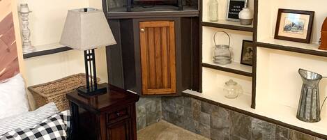 A cozy room with a fireplace, checkered bedding, and shelves with decorative items.