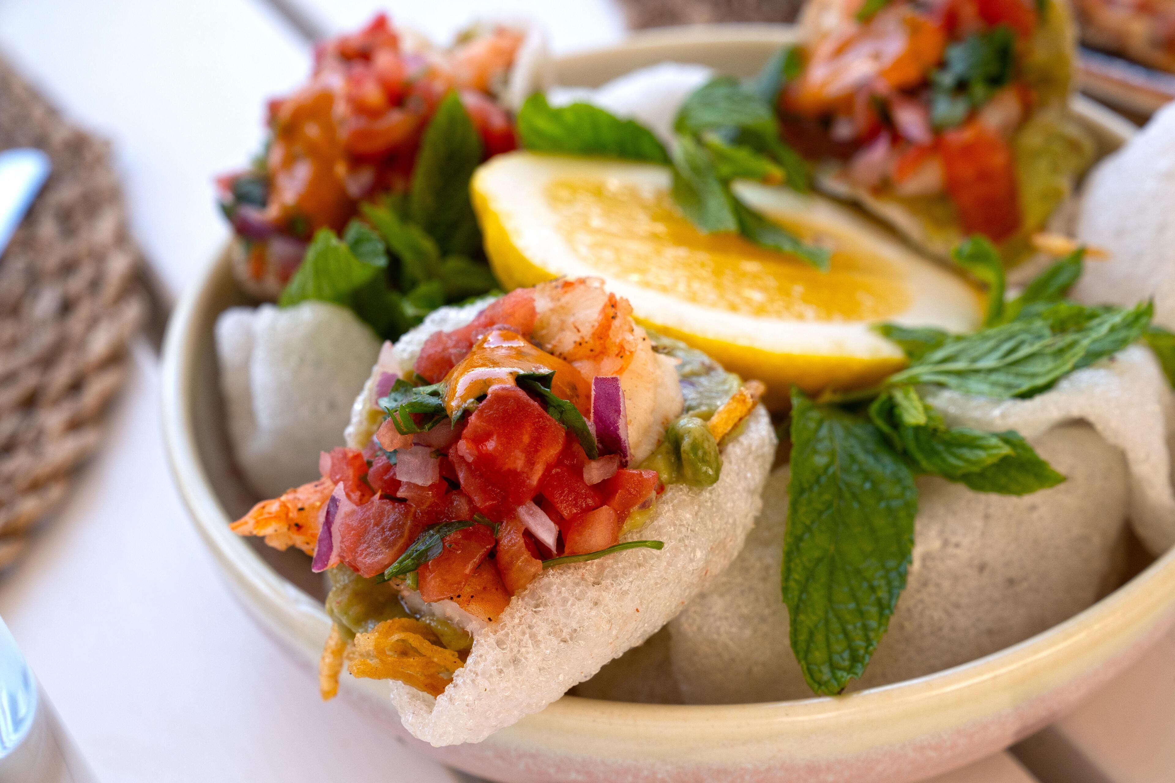 A bowl of spring rolls with fresh herbs and a slice of lemon.