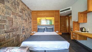 Un dormitorio moderno con pared de piedra, una cama grande con ropa de cama gris, un cabecero de madera y una mesita de noche con hervidor.