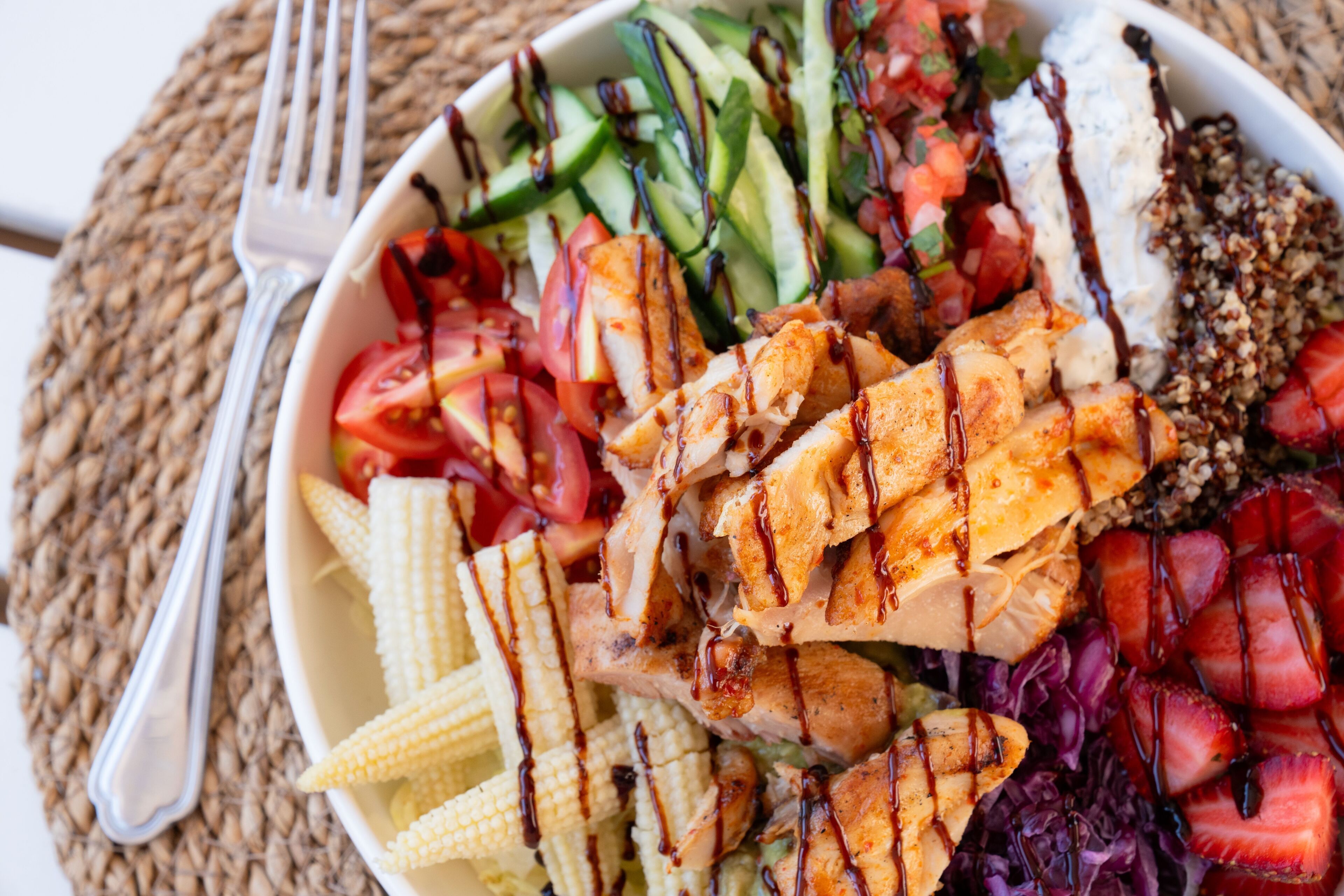 A bowl of salad with grilled chicken, vegetables, and a drizzle of sauce.