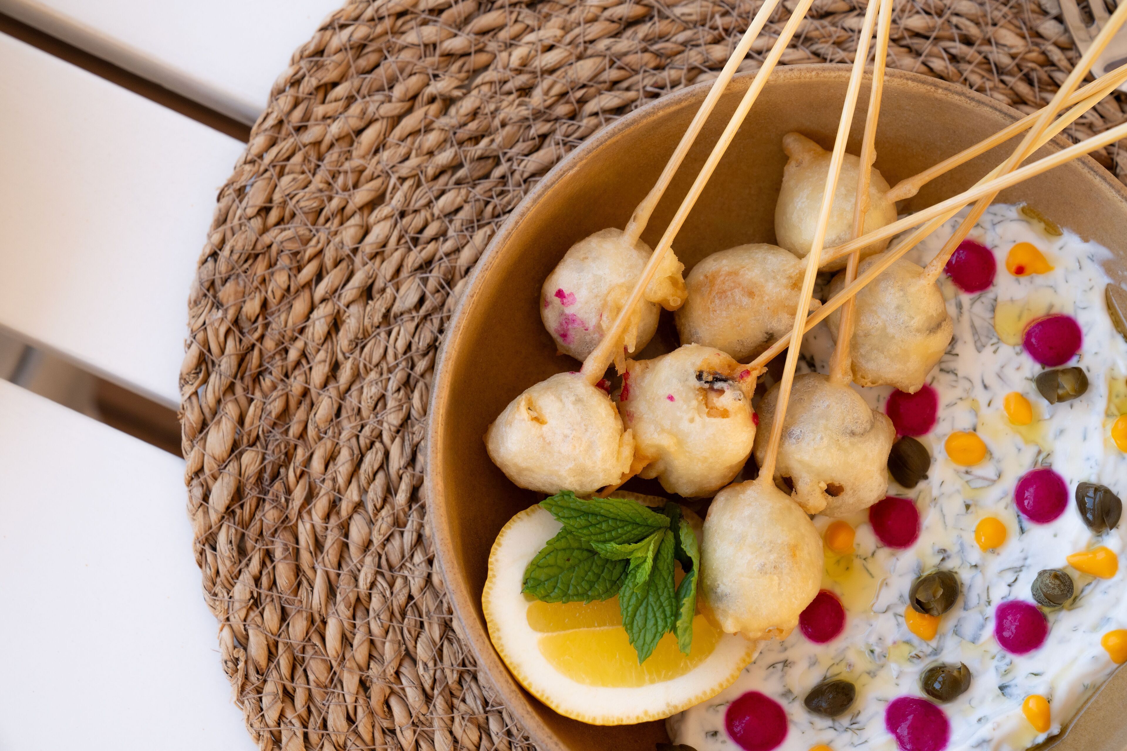 A bowl of food with skewers, a slice of lemon, and a mint leaf.