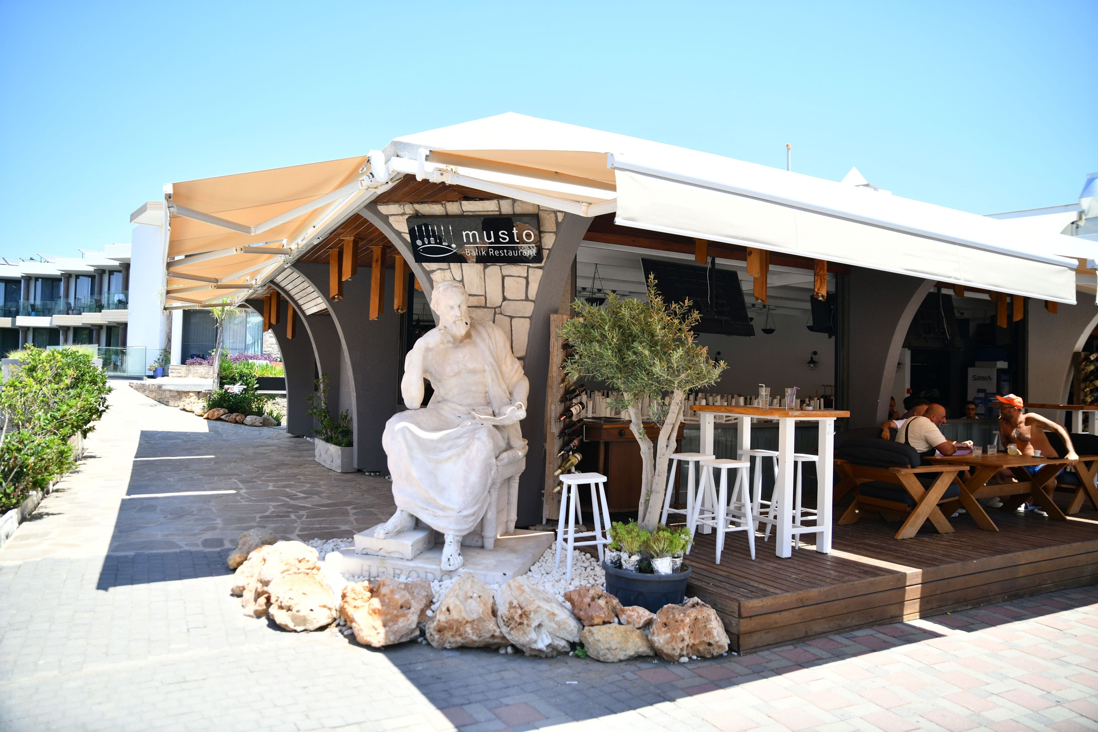 A restaurant named 'Musto' with outdoor seating, a statue, and a stone facade.