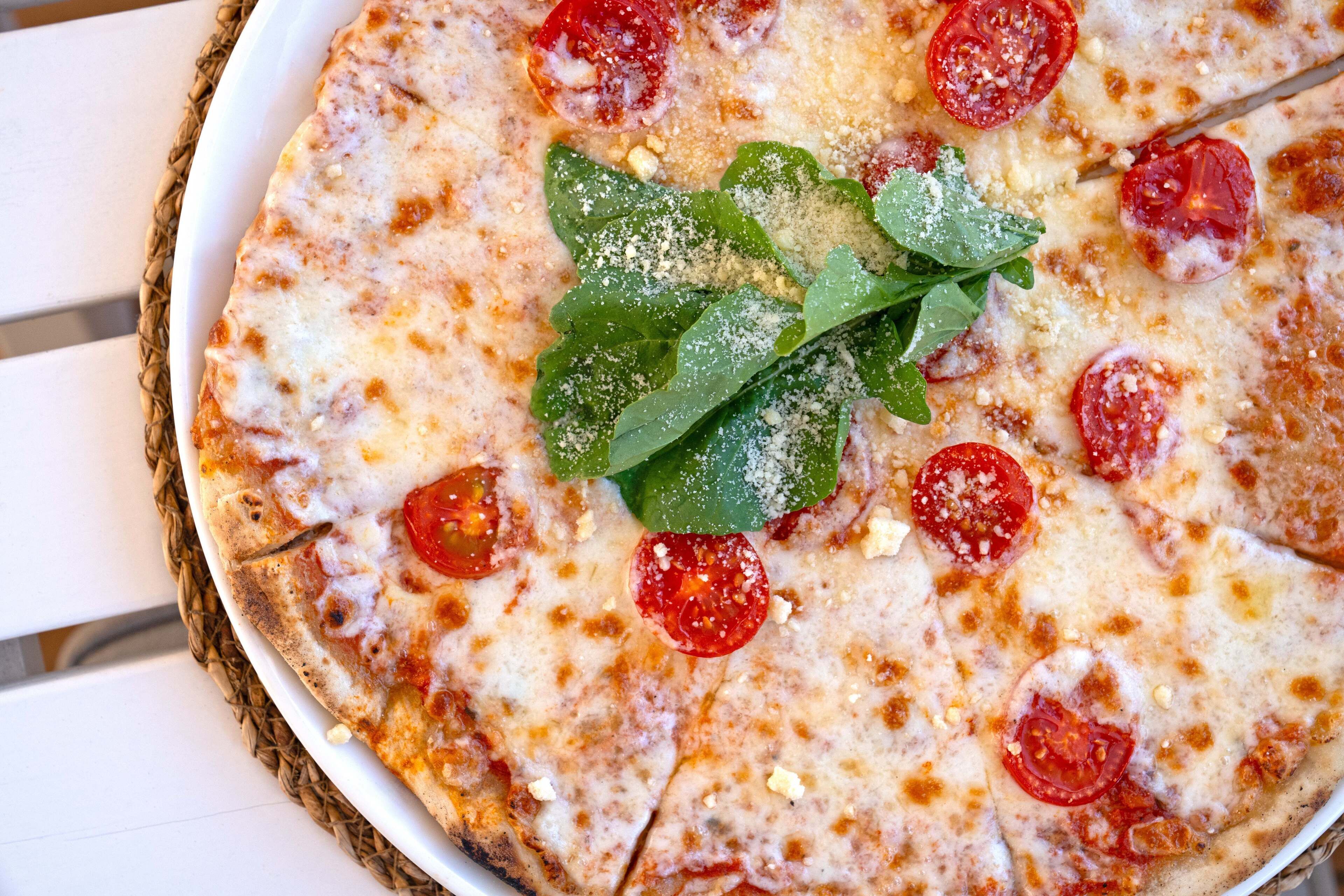 A pizza with tomato slices and basil leaves on a white plate.