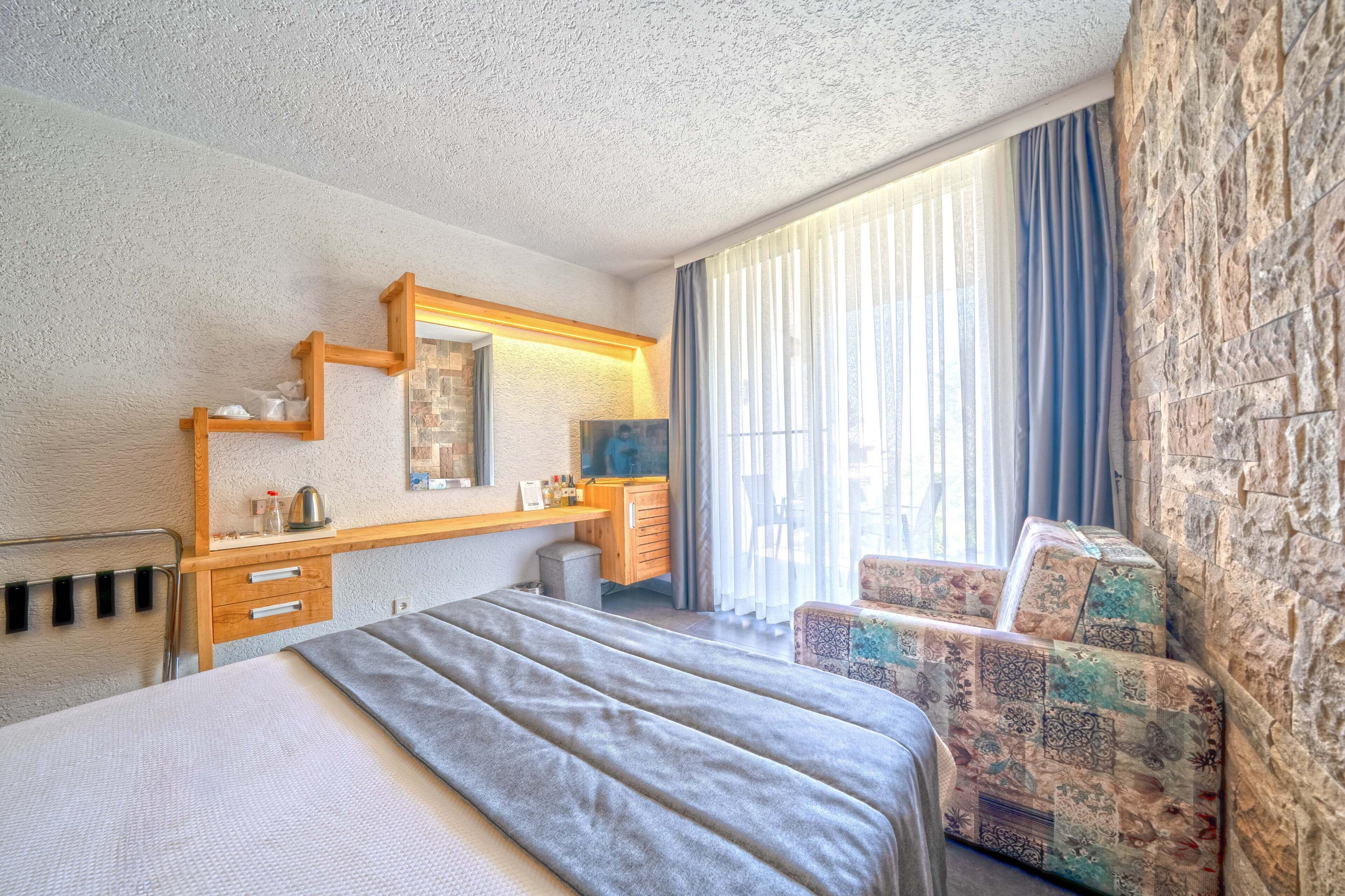 A hotel room with a bed, a wooden desk, a chair, and a large window with curtains.