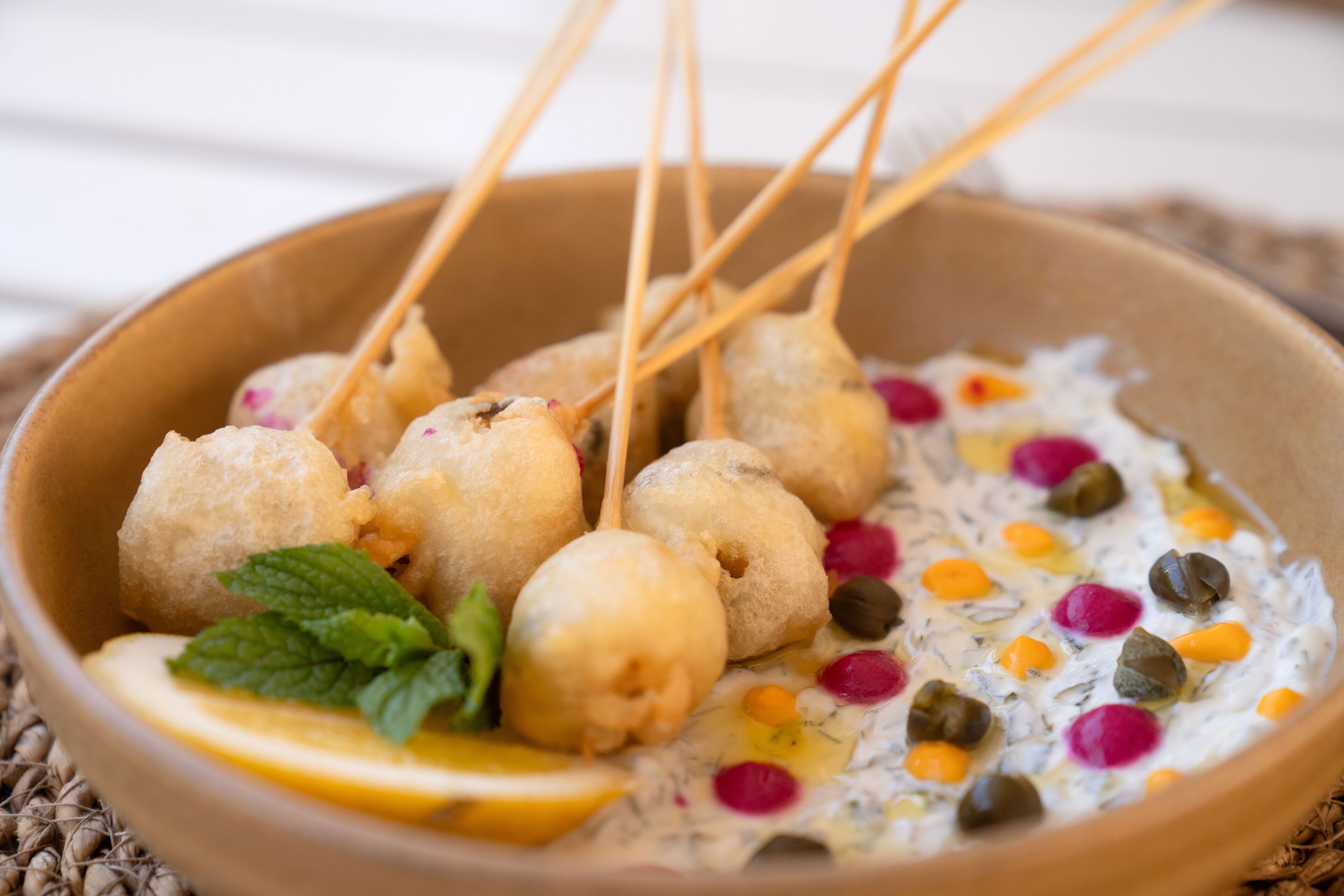 A bowl of food with skewered items and a creamy dip with colorful toppings.