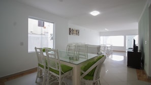 A spacious dining area with a glass-top table and white wicker chairs with green cushions.
