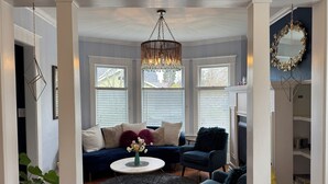 A living room with a dark blue sofa, a round coffee table with a vase, and a blue armchair. There is a chandelier hanging from the ceiling.