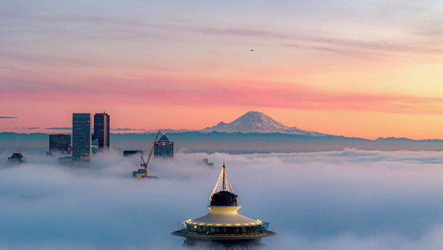 A cityscape with a prominent mountain in the background, surrounded by clouds.