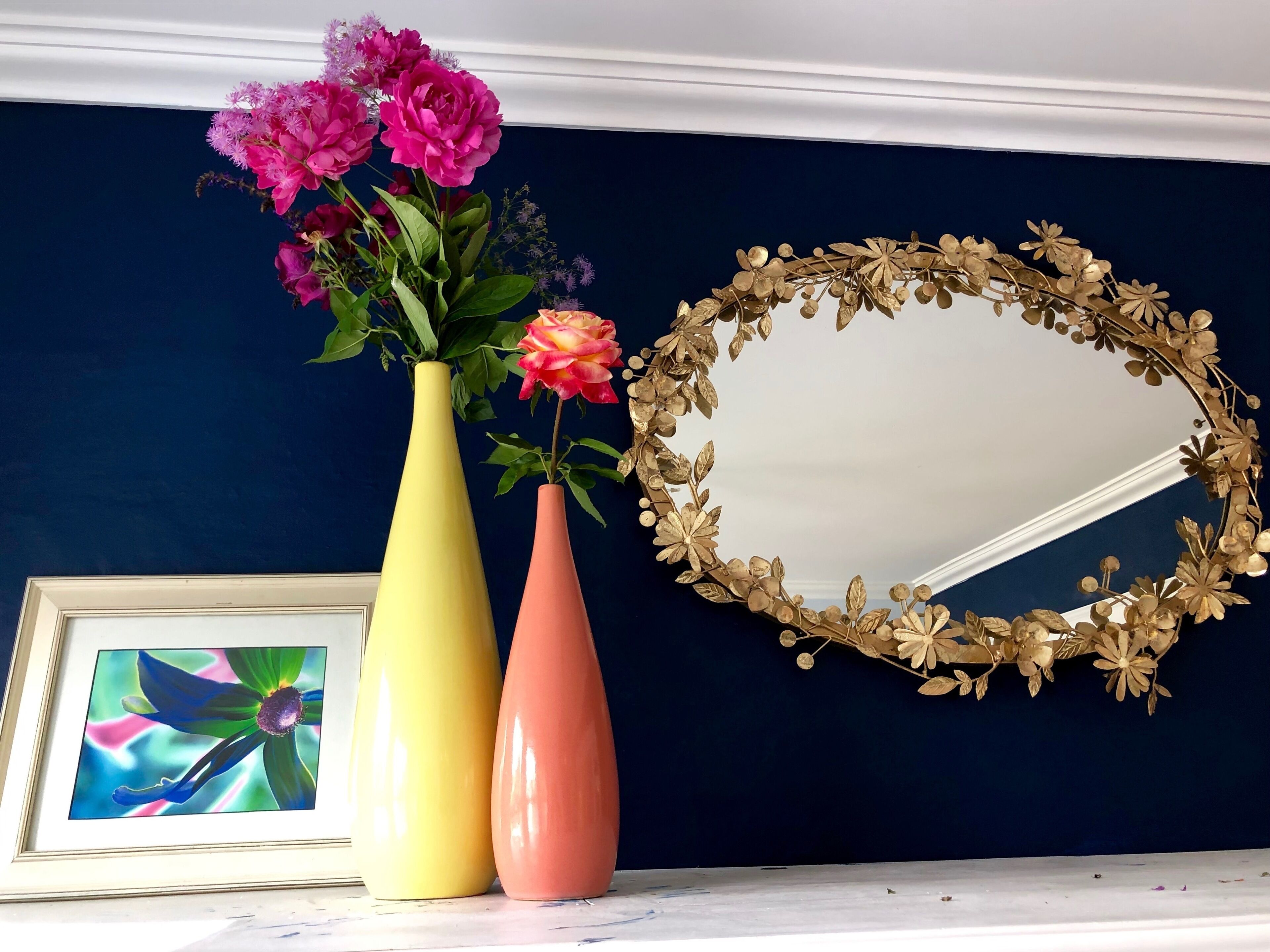 Two vases with flowers and a decorative mirror on a wall.