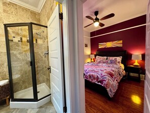 A bedroom with a bed, nightstands, a ceiling fan, and a shower area with glass doors.