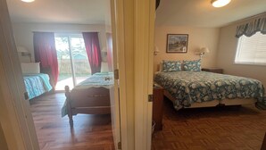 Une chambre avec un plancher en bois, un lit recouvert d’une couvre-lit à motifs floraux, une table de chevet et une fenêtre avec des stores.