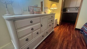 Une commode blanche avec de nombreux tiroirs et des boutons, un miroir au-dessus, et une lampe posée sur la commode.