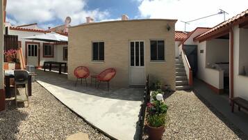A courtyard with a curved building, two red chairs, a bench, and potted plants.