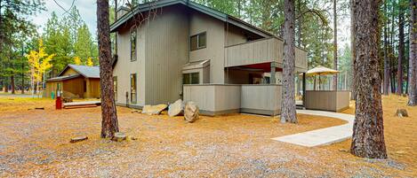 Situated in a forested area, this cabin offers a covered outdoor seating area with a view of the surrounding natural landscape.