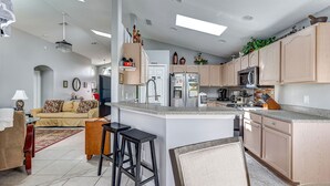 A modern kitchen with a central island, bar stools, and a dining area with a sofa and coffee table.
