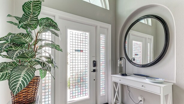 A hallway with a white door, a potted plant, a white console table, a round mirror, and a tiled floor.
