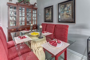 Un comedor con mesa de vidrio, sillas tapizadas en rojo, un aparador de madera con puertas de cristal, y dos cuadros enmarcados en la pared.