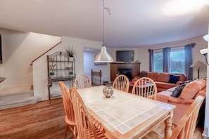 A cozy living room with a dining table, wooden chairs, a sofa, and a TV.