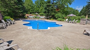 A swimming pool with a concrete deck, surrounded by lounge chairs and umbrellas.
