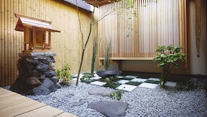 A traditional Japanese garden with a wooden deck, stone lantern, and bamboo fence.