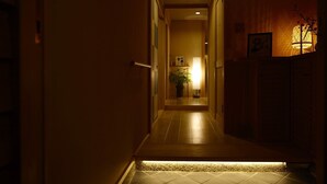 A narrow hallway with a tiled floor leading to a room with a bed, a bedside table, and a nightstand.