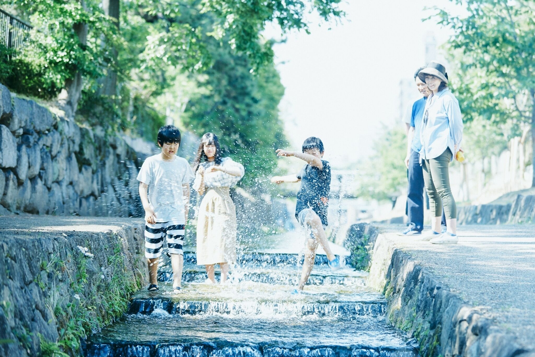 Un groupe de personnes joue à l’eau sur un chemin de pierre bordé de verdure.