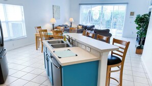 A kitchen with a central island, two sinks, and a dining area with chairs and a sofa.
