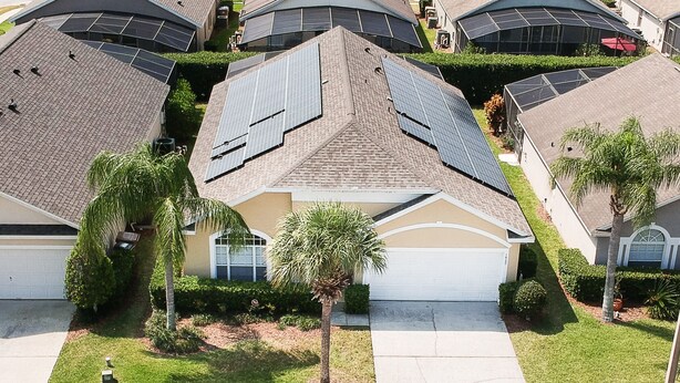 A residential area with houses featuring solar panels, a palm tree, and a well-maintained lawn.