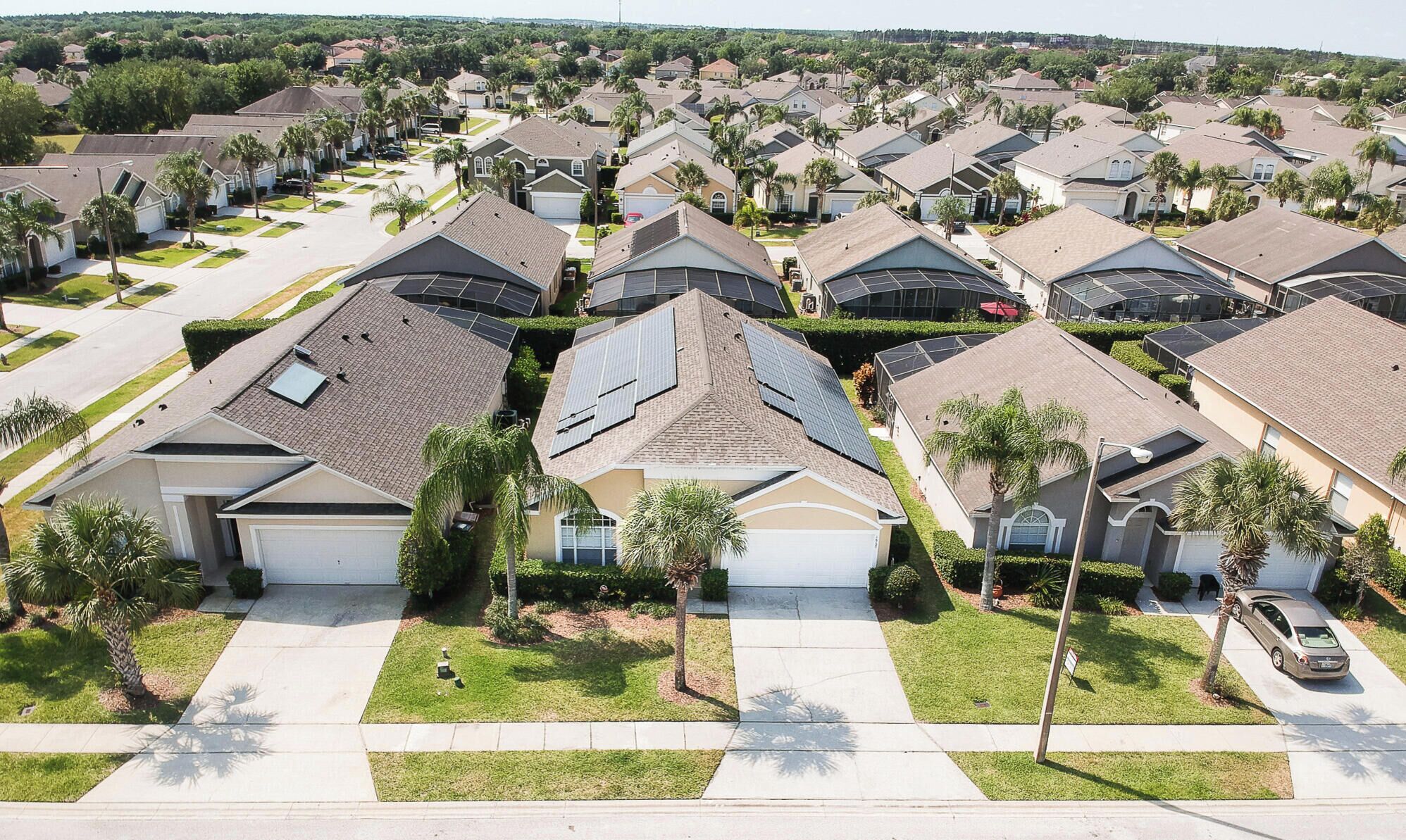 A residential area with houses featuring solar panels, a clear sky, and a well-maintained lawn.
