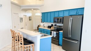 A kitchen with blue cabinets, a black refrigerator, and a central island with chairs.