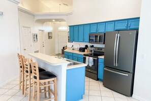 A kitchen with blue cabinets, a black refrigerator, and a central island with chairs. - Solar Powered Villa Near Disney, South Pool/Spa (Clermont)