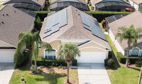A residential area with houses featuring solar panels, a palm tree, and a well-maintained lawn. - Solar Powered Villa Near Disney, South Pool/Spa (Clermont)