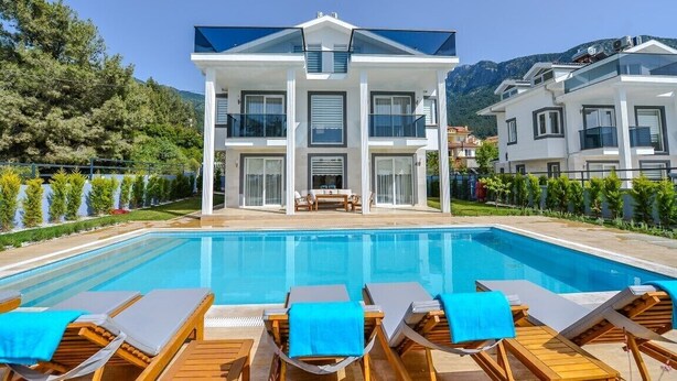 Un hotel moderno con piscina, sillones de madera y vistas a las montañas.
