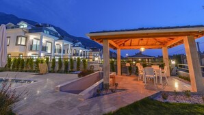 Un patio exterior moderno con pérgola, mobiliario y piscina.